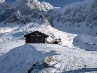 there are snow - covered hills and mountains behind the small hut that the skiers sit in