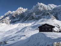 there are snow - covered hills and mountains behind the small hut that the skiers sit in