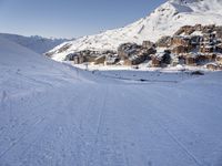 an empty snowy mountain area with buildings on it and skiiers in the foreground