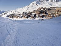 an empty snowy mountain area with buildings on it and skiiers in the foreground