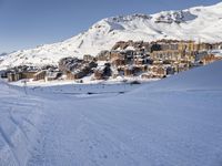 an empty snowy mountain area with buildings on it and skiiers in the foreground