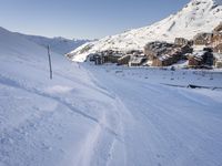 an empty snowy mountain area with buildings on it and skiiers in the foreground