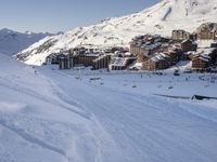 an empty snowy mountain area with buildings on it and skiiers in the foreground