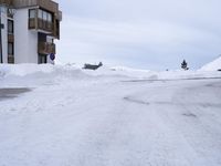 there is a snow bank next to the building where the street is located with it's cars