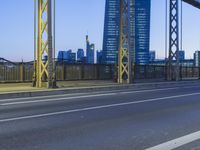 the underside of a steel bridge at dusk, with city buildings in the background at night