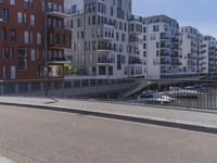 there is a man in white jacket walking along a bridge near water and buildings with boats