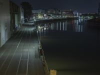 view of an empty train track on the side of the water at night time, with a long pier in the foreground