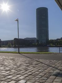a city scene with a large tower and a lake in the foreground and a person sitting on a bench with an umbrella near it