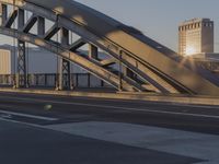 the cars on the street are driving under an arch bridge at sunset time, the sun has just broken