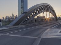 the sun is setting over the roadway in front of the bridge crossing river bank with downtown skyline behind