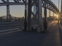 the sun shines behind an overpass with a large bridge in the background, with buildings in the distance