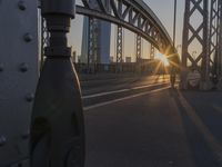 the sun shines behind an overpass with a large bridge in the background, with buildings in the distance