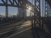 the sun peeks through a gap in the metal framework of the bridge over water