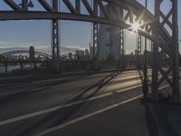 the sun peeks through a gap in the metal framework of the bridge over water