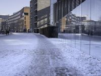 there are people walking on the street in the snow outside the glass building that is not yet finished