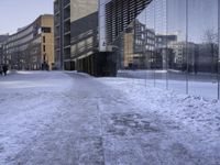 there are people walking on the street in the snow outside the glass building that is not yet finished