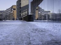 there are people walking on the street in the snow outside the glass building that is not yet finished