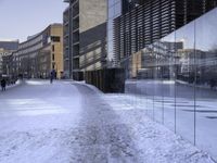 there are people walking on the street in the snow outside the glass building that is not yet finished