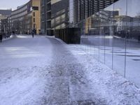 there are people walking on the street in the snow outside the glass building that is not yet finished