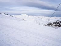 snow covered slope in the middle of a ski area as people ski on it near ski lift