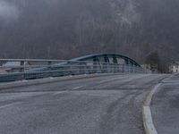 a long blue train traveling through a bridge next to trees and a mountain slope of mountains