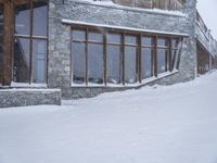 a snowboarder in a blue jacket and brown hat going down the mountain with a wooden lodge behind them