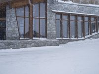 a snowboarder in a blue jacket and brown hat going down the mountain with a wooden lodge behind them