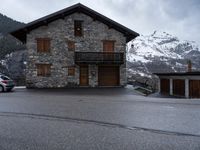 a small house sitting beside the road next to a building on a mountain top near the snow capped mountains