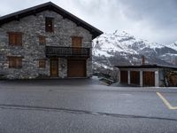 a small house sitting beside the road next to a building on a mountain top near the snow capped mountains