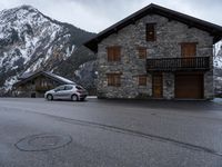 a small house sitting beside the road next to a building on a mountain top near the snow capped mountains