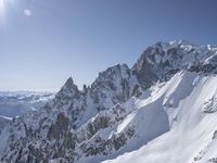 a lone skier on a steep, snowy mountain range in the background is snow and the sun