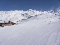 a mountain with some snow and a snowy hill with mountains behind it and skiiers in the foreground