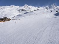 a mountain with some snow and a snowy hill with mountains behind it and skiiers in the foreground