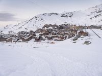 a person is standing on the ski slope near the snow covered mountain village that's surrounded by a line of cable cars