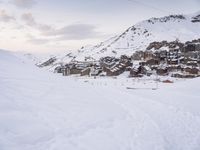 a person is standing on the ski slope near the snow covered mountain village that's surrounded by a line of cable cars