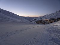 a ski lodge sits in the middle of a large mountain at night with tracks all over the snow