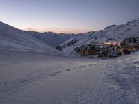 a ski lodge sits in the middle of a large mountain at night with tracks all over the snow