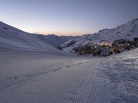 a ski lodge sits in the middle of a large mountain at night with tracks all over the snow