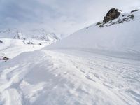 a person riding skis down a snow covered slope near snow covered mountain tops with steeply slope