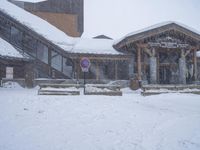 a snowy mountain scene with benches in the snow and a building with glass windows behind it