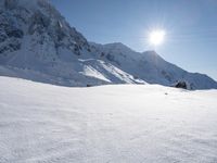 a skier is heading down a snowy mountain path in the sun, with mountains in the background