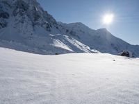 a skier is heading down a snowy mountain path in the sun, with mountains in the background