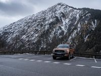 the orange truck is driving past a mountain of snow - covered mountains on the road