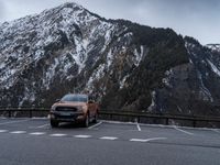 the orange truck is driving past a mountain of snow - covered mountains on the road