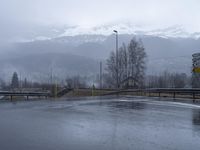 a large street corner is shown covered in rain and some snow on the mountains as seen from a small bridge