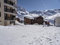 three skiers skiing down a slope by a resort building with balconies and balconies