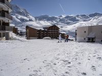 three skiers skiing down a slope by a resort building with balconies and balconies