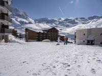 three skiers skiing down a slope by a resort building with balconies and balconies