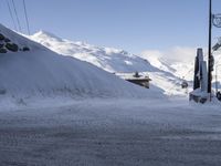 a snowy road in front of the snow - capped mountains with ski lift and lodge nearby