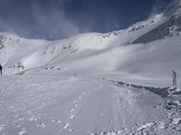 a mountain with people on skis and snowboards in the foreground, one on a cross country trail in front of the other